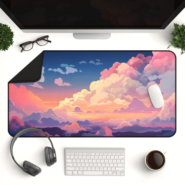 Home Decor - A desktop setup includes a monitor, keyboard, mouse, headphones, coffee cup, potted plants, and glasses. The Cloud Desk Mat – Cute Large Mouse Pad for Gaming & Office Setup showcases a colorful, dreamy sky with fluffy clouds and a sunset. Embracing kawaii aesthetics, the scene is vibrant with shades of pink, orange, and blue. - Kaladyn Designs