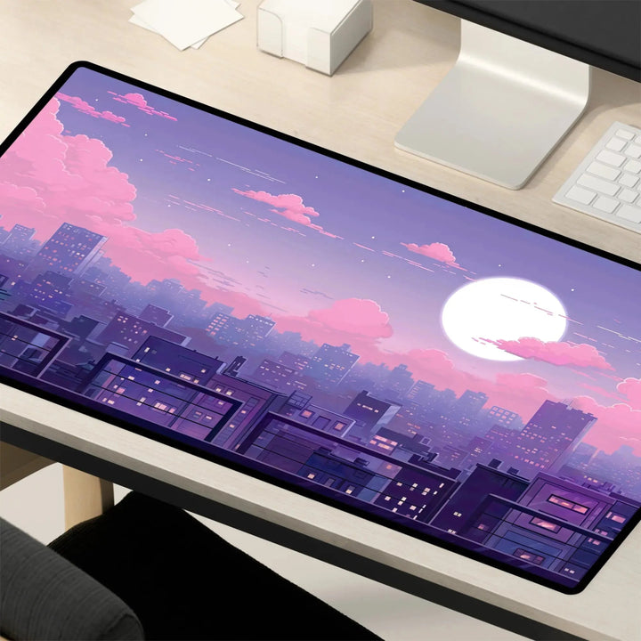 A computer monitor on a Kawaii Desk Mat – Lofi Vaporwave Pixel Art Anime Mouse Pad for Gaming & Work displays a digital artwork of a city skyline at dusk. The sky is filled with shades of pink and purple, dotted with clouds. A large, bright moon is visible, casting a serene glow over the buildings. A keyboard and other items are nearby.