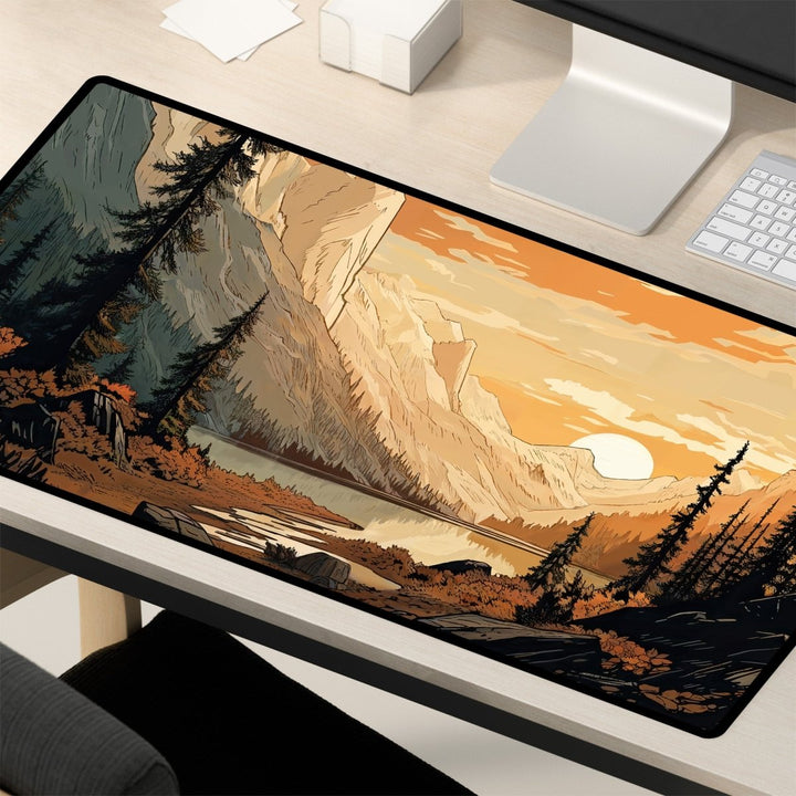 Home Decor - A desk setup featuring the Mountain Desk Mat – Large Nature Desk Mat for Gaming & Office, with a scenic forest and valley design showcasing a picturesque mountainous area, river, and trees in the foreground. The backdrop depicts a sunset with an orange sky. This nature - inspired decor includes a white keyboard, monitor, and part of a chair. - Kaladyn Designs