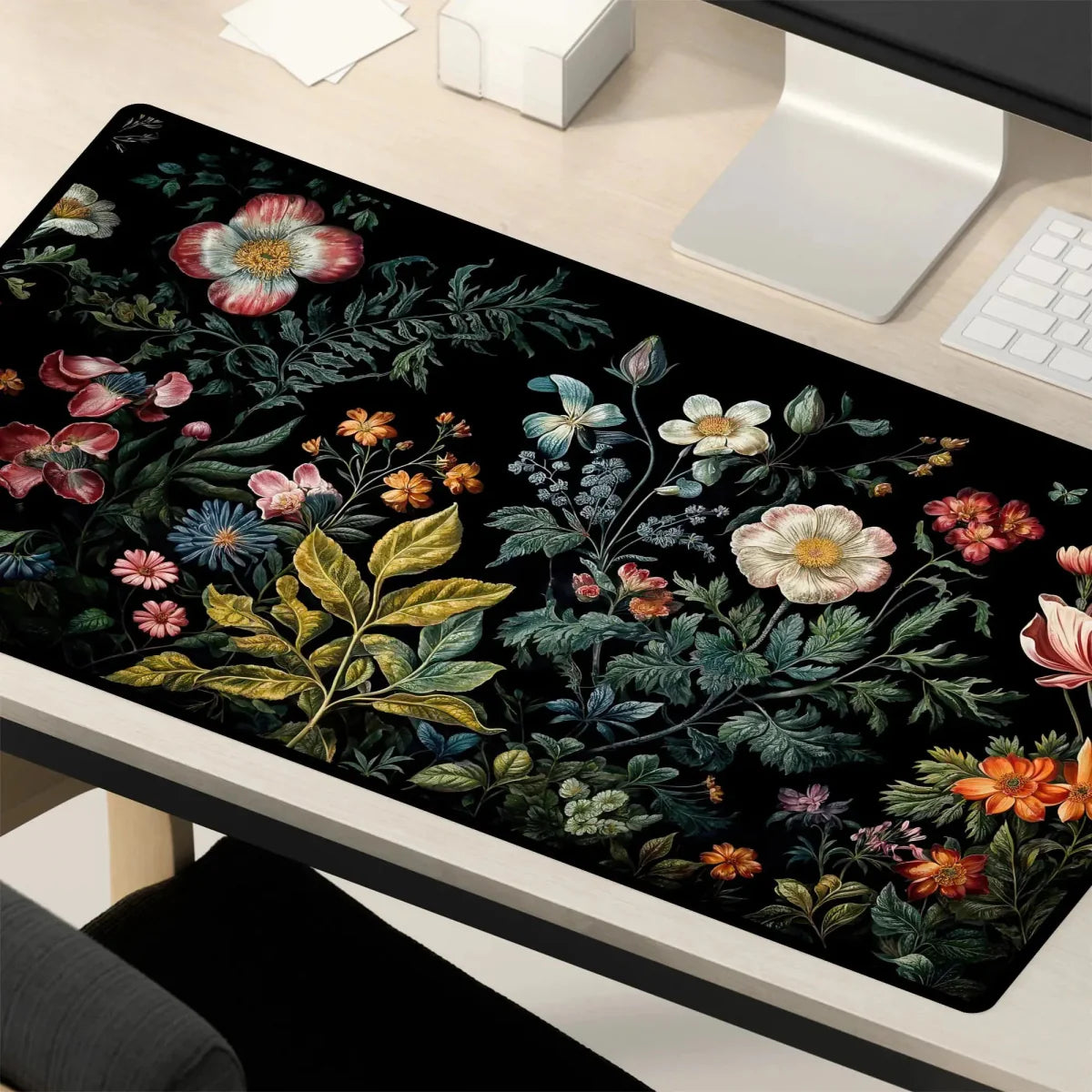 Desk mat featuring a detailed floral design with various colorful flowers and greenery on a black background, placed on a modern desk alongside a computer monitor and keyboard.