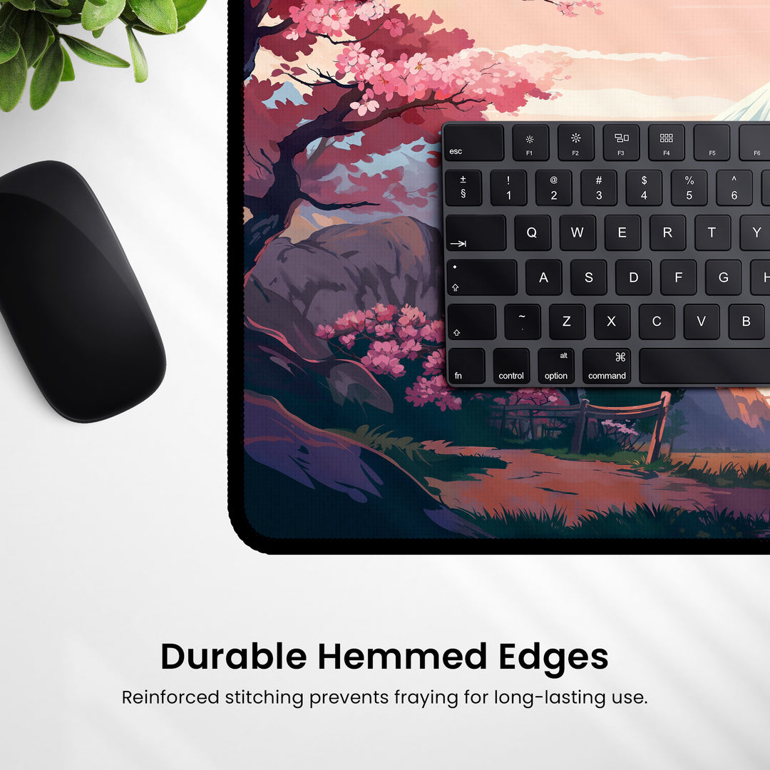 A desk setup showcasing a black mouse and partial keyboard sits on the delightful Cherry Blossom Anime Desk Mat, adorned with a scenic illustration of cherry blossoms and mountains. The product emphasizes its "durable hemmed edges" for extended use, adding kawaii aesthetics to your workspace.