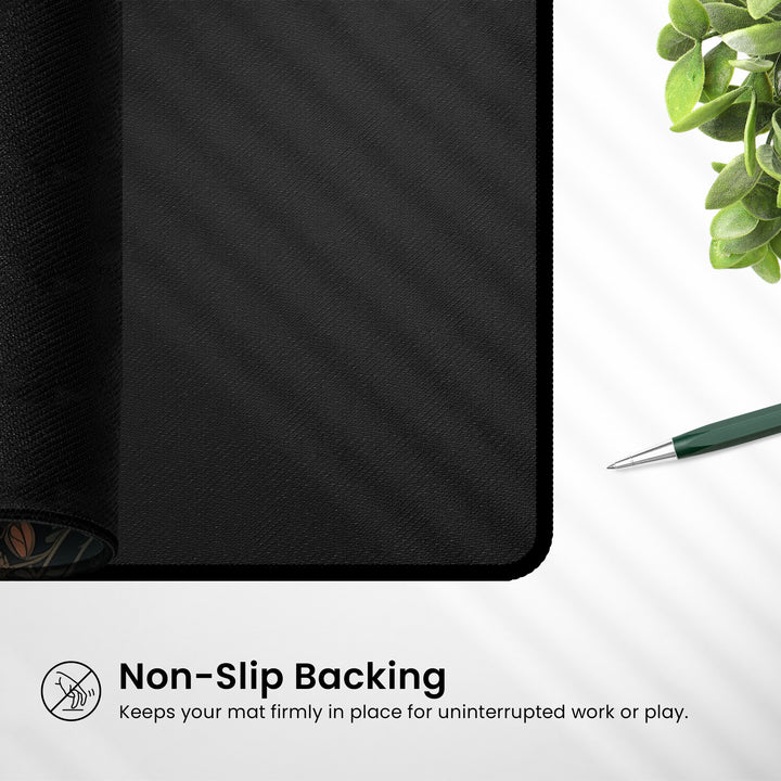 A Cherry Blossom Anime Desk Mat with a non-slip backing is featured. Below, the text reads, "Non-Slip Backing: Ensures your mat stays securely in place for seamless work or play." Nearby, a green plant and a pen enhance the kawaii aesthetics on a white surface.