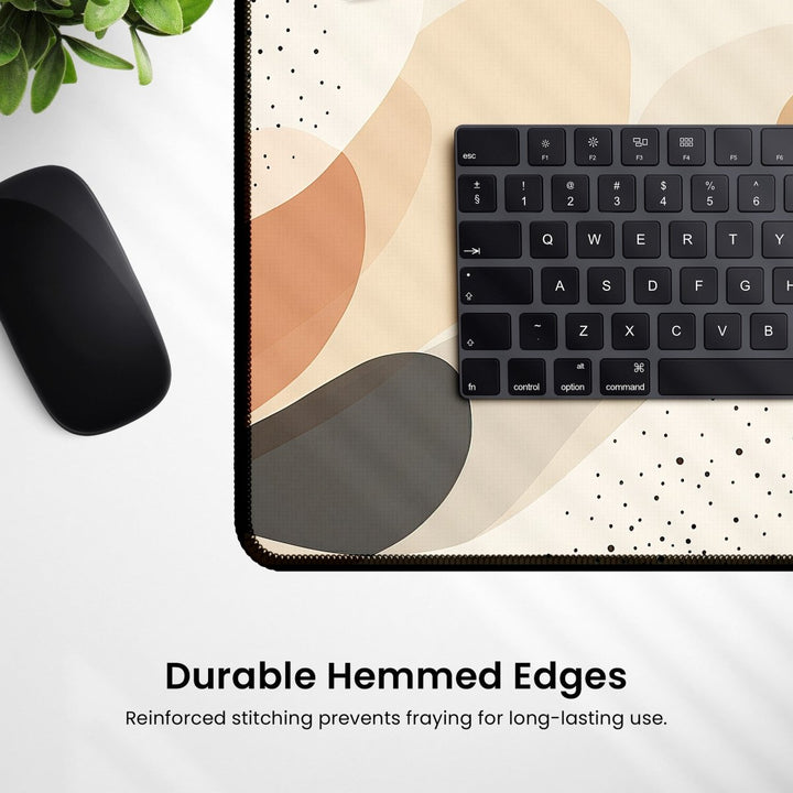Home Decor - A minimalist desk setup showcases a dark keyboard and mouse on the Cute Boho Desk Mat – a large, beige pad with an abstract pattern that enhances modern workspaces. Text highlights "Durable Hemmed Edges. Reinforced stitching prevents fraying for long - lasting use." A small plant in the corner adds a natural element to the design. - Kaladyn Designs