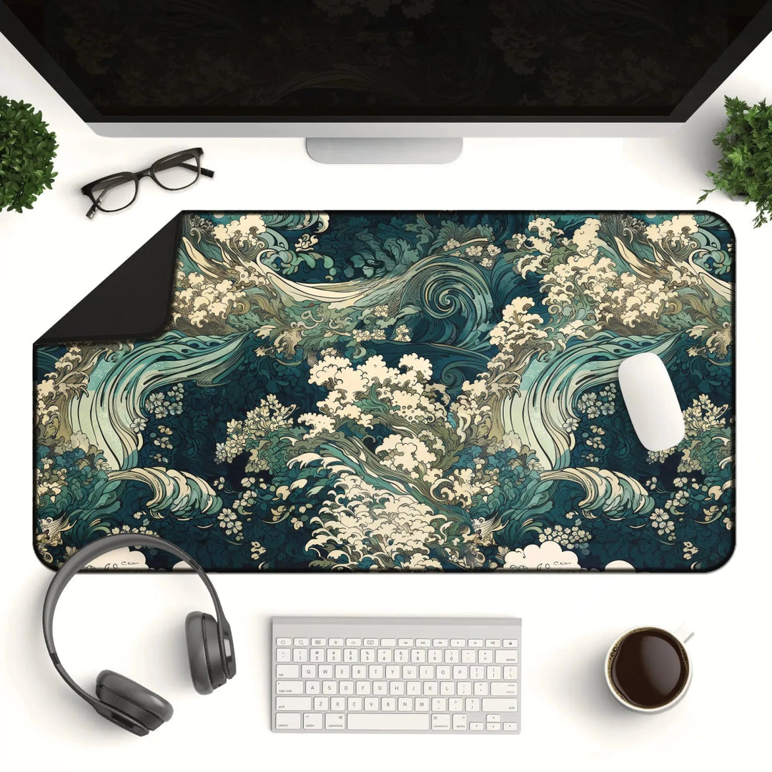 A well-organized computer desk setup featuring the Japanese Ukiyo-e Inspired Desk Mat – a large neoprene gaming mouse pad and office decor with a wave pattern, along with a pair of glasses, a monitor, keyboard, mouse, headphones, a potted plant for added workspace ambiance, and a cup of coffee. The design pays homage to traditional Japanese art with its depiction of turbulent waves.