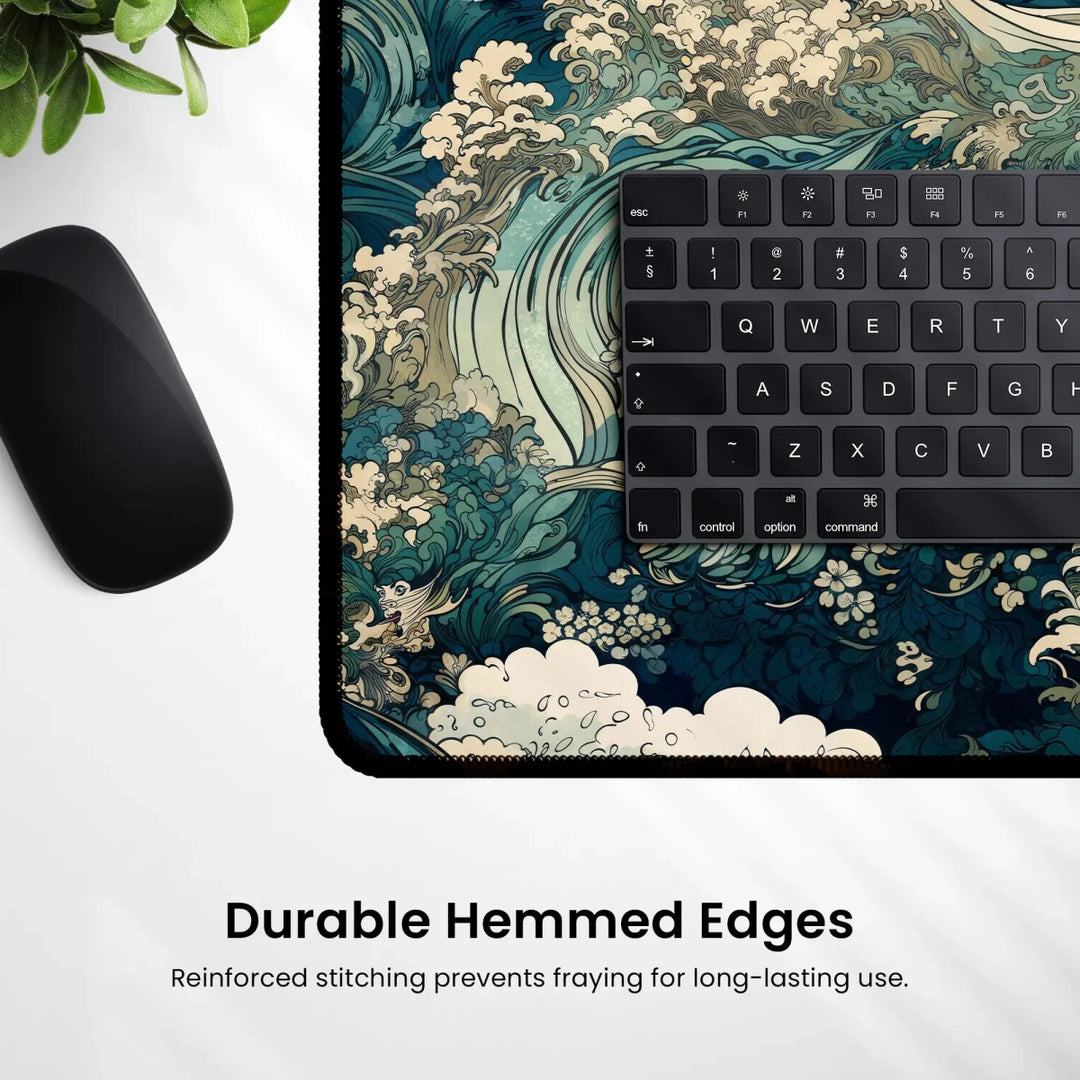 A close-up view of a desk highlights a keyboard and the Japanese Ukiyo-e Inspired Desk Mat, a large neoprene gaming mouse pad adorned with an ocean wave design reminiscent of traditional Japanese art. Text at the bottom reads, "Durable Hemmed Edges - Reinforced stitching prevents fraying for long-lasting use." A small plant in the top left corner enhances the workspace decor.