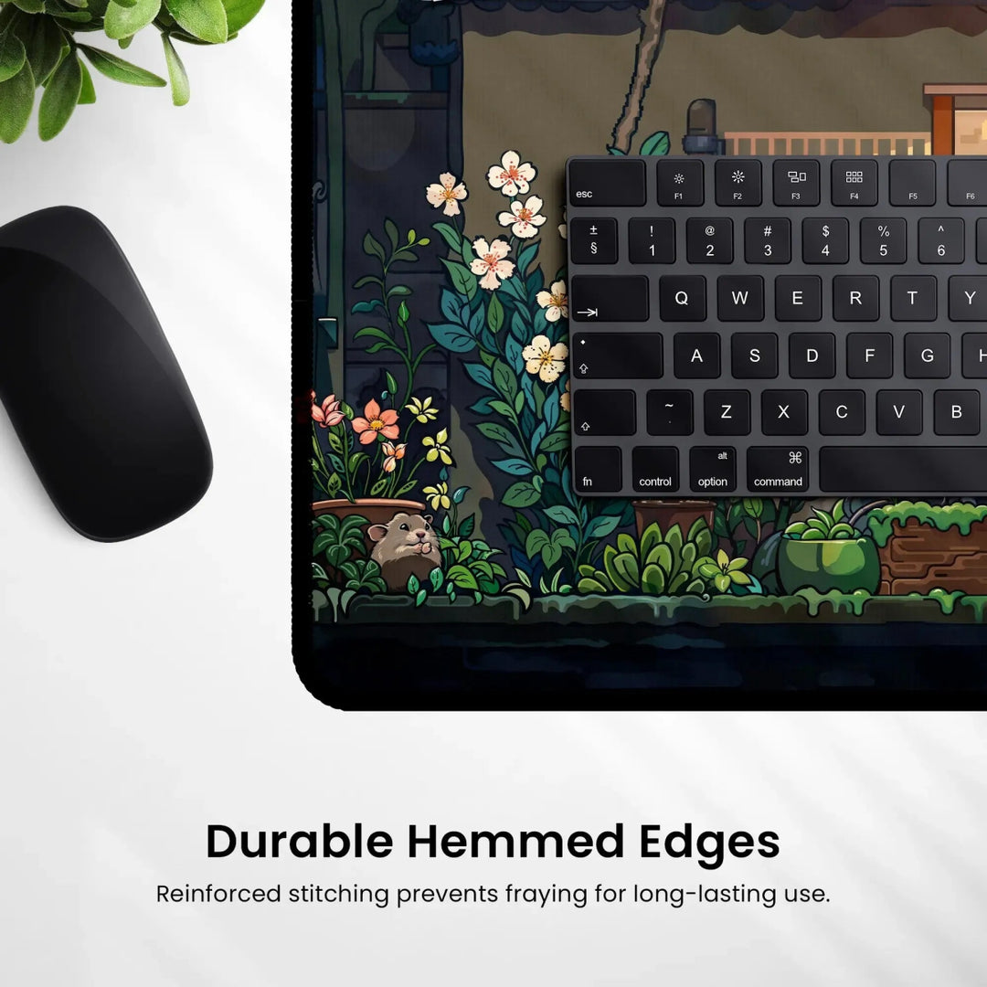 The Kawaii Desk Mat – Cute Japanese Anime Design Non-Slip Mouse Pad for Gamers showcases a whimsical garden scene with flowers and a small mouse character in an enchanting Japanese anime style. On the right side of the mouse pad, there’s a partial view of a black keyboard. Below, the text reads "Durable Hemmed Edges" and highlights reinforced stitching to prevent fraying.