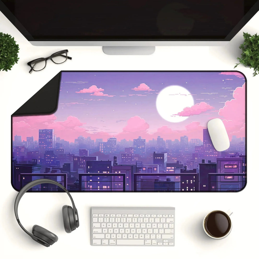 A stylish desktop setup features a keyboard, mouse, monitor, headphones, glasses, and a cup of coffee. The Kawaii Desk Mat – Lofi Vaporwave Pixel Art Anime Mouse Pad for Gaming & Work showcases a vibrant cityscape at sunset with a large moon and purple sky, creating a serene and aesthetic work environment.