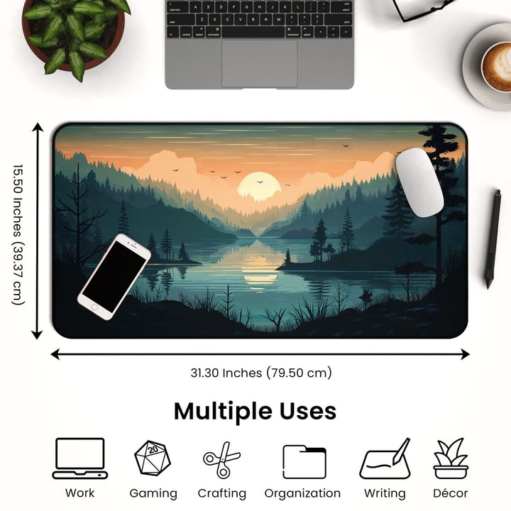 Home Decor - A Mountain Desk Mat - Large Nature - Inspired Mouse Pad for Gaming & Office, measuring 31.30 x 15.50 inches, features a picturesque scene of a sunset over a lake and forest. On the white table around the mat, you'll find a laptop, phone, mouse, plant, and coffee cup. Icons below highlight its diverse applications. - Kaladyn Designs