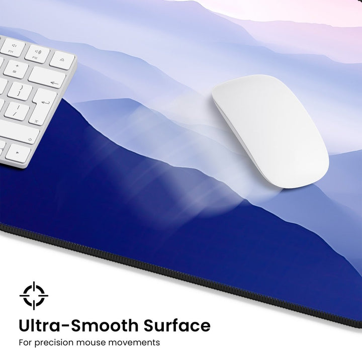 Home Decor - A white keyboard and mouse rest on the large Mountain Desk Mat, a premium neoprene mouse pad adorned with a smooth, abstract blue and purple mountain design. The text in the bottom left corner reads, "Ultra - Smooth Surface for precision mouse movements," creating a tranquil workspace ideal for both office or gaming setups. - Kaladyn Designs