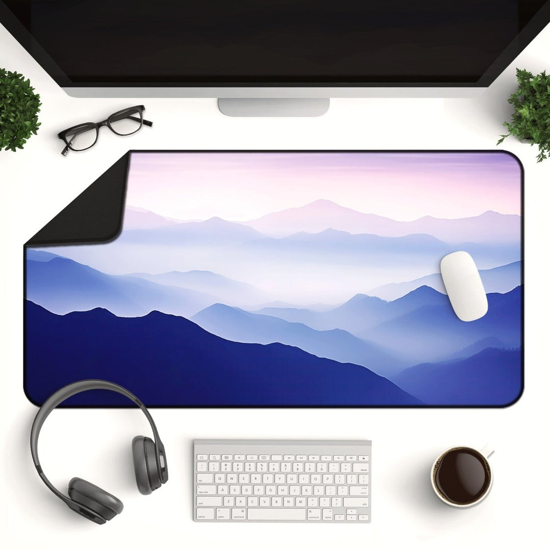 Home Decor - A computer monitor on a white desk with the Mountain Desk Mat – Large Nature Mouse Pad for Office or Gaming Setup, featuring a serene mountain landscape. An Apple Magic Mouse rests on the mountain desk mat. The setup includes a keyboard, headphones, a cup of coffee, eyeglasses, and small potted plants on either side of the monitor. - Kaladyn Designs