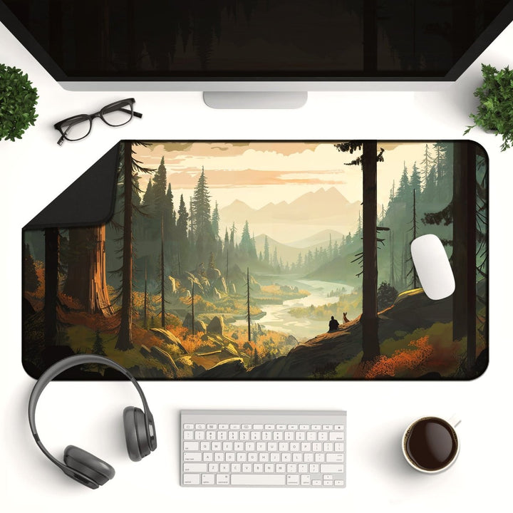 Home Decor - A desktop setup featuring a Mountain Desk Mat – Large Nature Mousepad for Gaming & Office, Forest and Valley Decor, illustrated with a forest, mountains, and a river. On the desk are gaming accessories like a keyboard, mouse, headphones, glasses, a coffee cup, and two small plants, with a large monitor in the background. - Kaladyn Designs