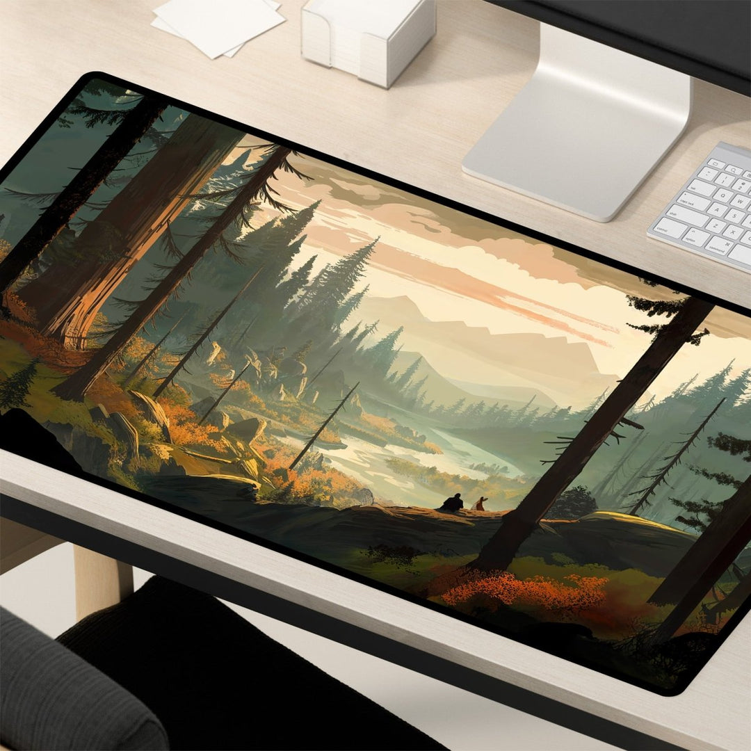 Home Decor - A desk with a computer monitor, keyboard, and a large Mountain Desk Mat – Large Nature Mousepad for Gaming & Office, Forest and Valley Decor. The mat depicts a river flowing through a dense forest with tall trees and mountains in the background, under a sky painted in warm sunset hues. - Kaladyn Designs