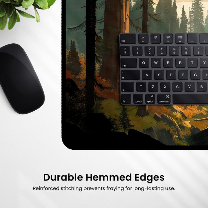Home Decor - A black computer keyboard and mouse rest on a Mountain Desk Mat – Large Nature Mousepad for Gaming & Office, featuring a forest and valley decor. A plant is partially visible in the top left corner. Text at the bottom reads, "Durable Hemmed Edges - Reinforced stitching prevents fraying for long - lasting use. - Kaladyn Designs