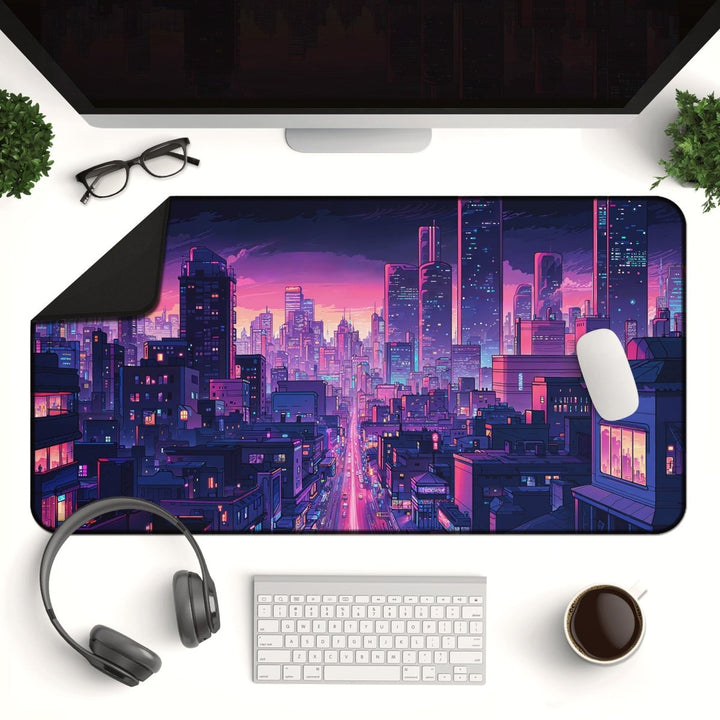 Home Decor - A computer desk setup featuring a monitor, glasses, headphones, keyboard, and a coffee cup includes the Neon City Desk Mat - Anime Gaming Mouse Pad & Vaporwave Aesthetic Decor, which showcases a colorful cityscape with skyscrapers and a vibrant sunset. - Kaladyn Designs